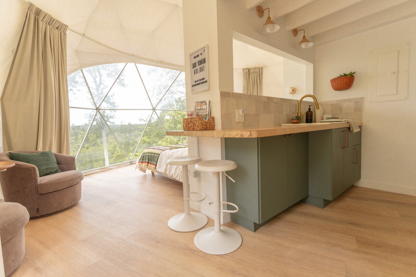 Dome interior with curved geodesic window, lounge chair, and kitchen at Short Mountain Holiday