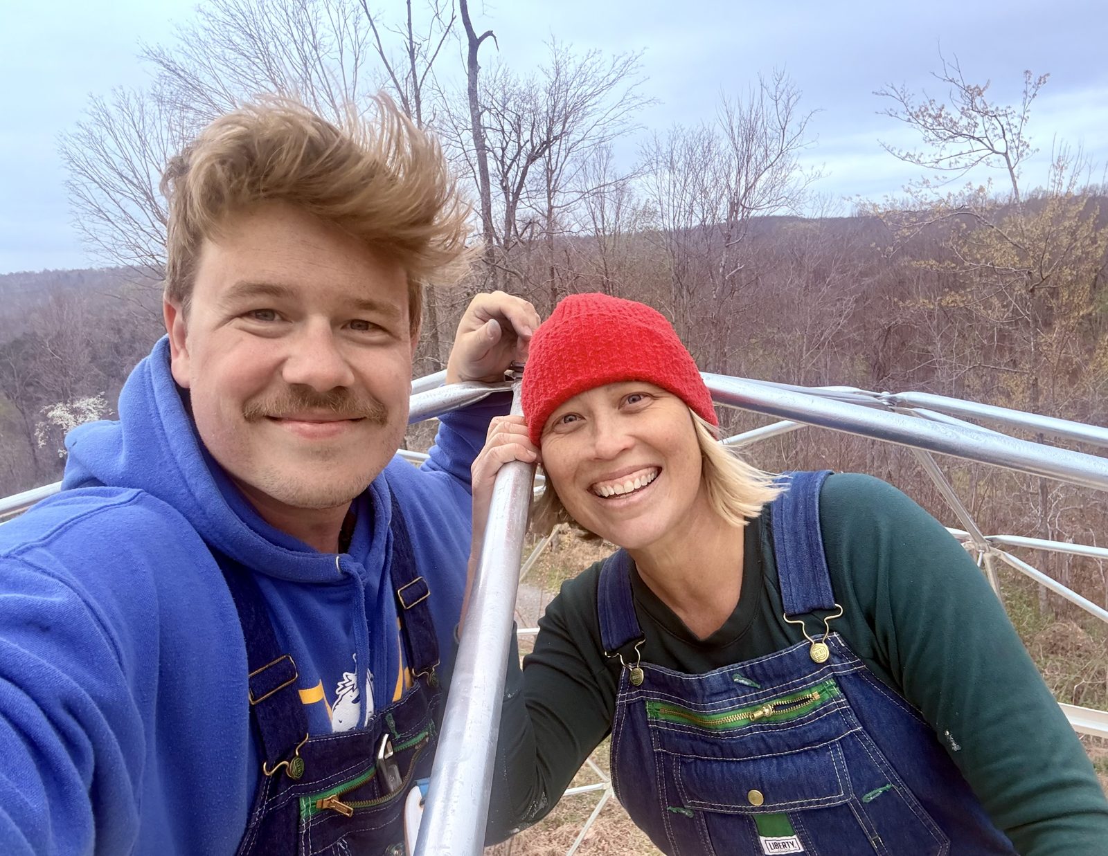 Micah and Amber, the owners of Short Mountain Holiday, smiling inside a geodesic dome frame on the mountain
