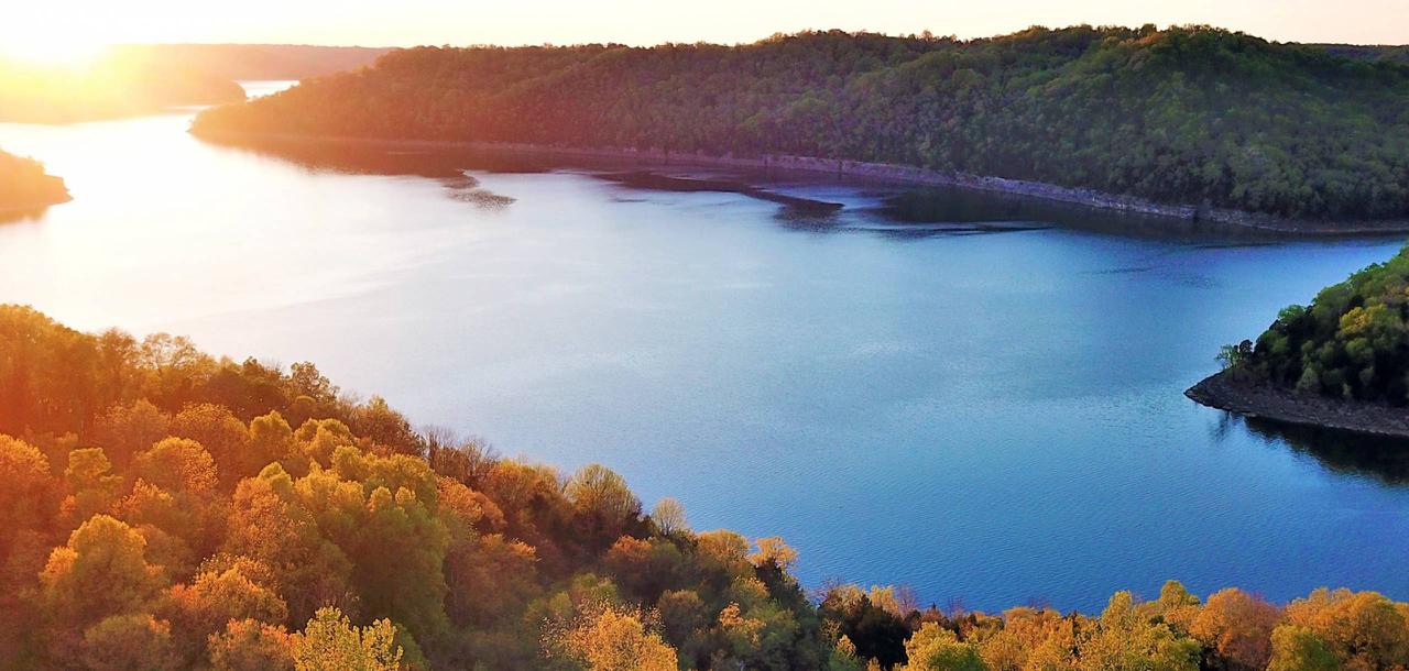 Aerial view of Center Hill Lake at golden hour — sunlight raking across the water with fall-colored ridges on both shores
