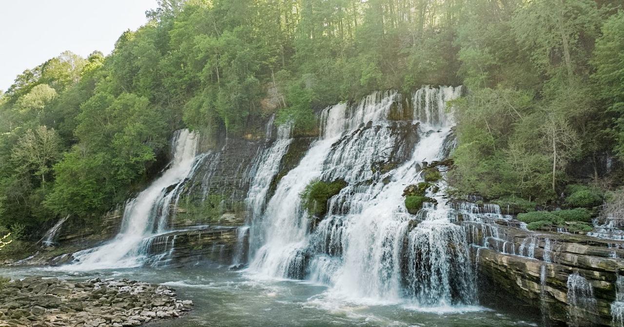 Twin Falls at Rock Island State Park — a wide cascade tumbling over a layered limestone cliff into the river below, surrounded by deep green forest